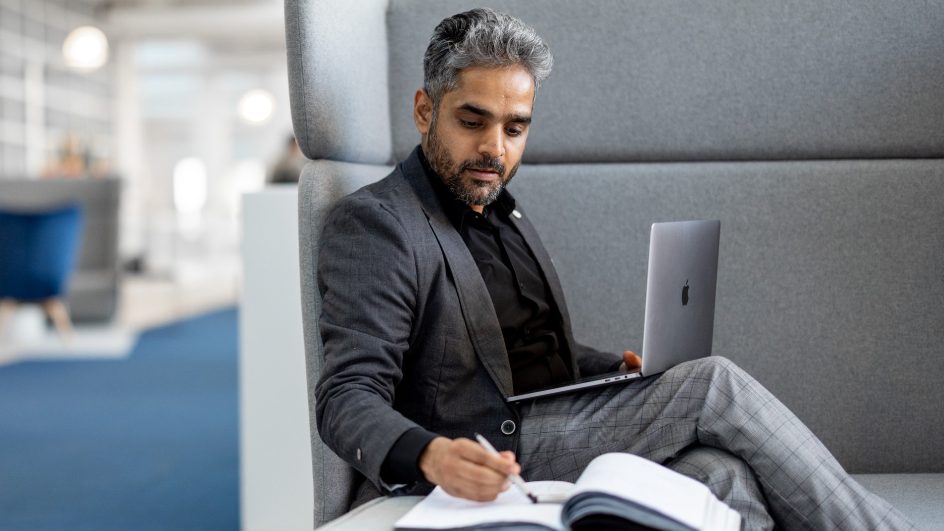 Ein Mann sitzt auf einem grauen Sofa und schaut in seinen Laptop
